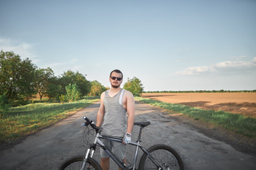 young cyclist man stands with his mountain bike and looking in to the camera. young man traveller stand on the road with his bicycle