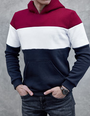 young man in red, white and blue color hoodie standing outdoors on gray background