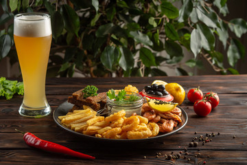 glass of foamy beer and a plate with snacks on a wooden background