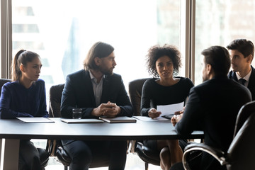 Confident African American businesswoman hr manager asking questions to candidate on job interview, holding resume cv, four recruiters sitting at table in boardroom, looking at job applicant