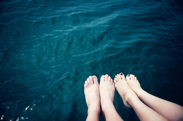 Female and male feet against blue water of the sea. Summer day in vacation..