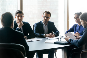 Serious confident businesspeople listening to mentor leader at meeting in boardroom, sitting at table at briefing, business partners colleagues discussing project strategy, contract terms