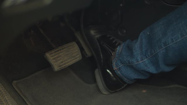 Close-up of male leg in trendy black leather shoe pressing brake pedal for emergency stop during driving car in the city.