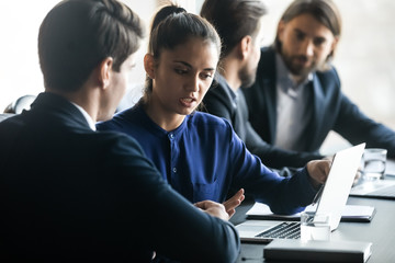 Confident businesswoman mentor training intern, using laptop, sitting at table in boardroom, team...