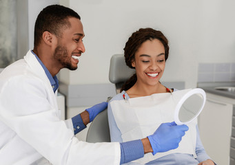 Friendly black dentist giving mirror to his happy patient
