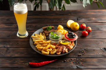 glass of foamy beer and a plate with snacks on a wooden background
