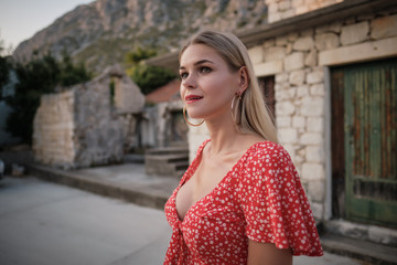 Fototapeta premium Vogue style elegant portrait of beautiful fashion woman wavy shine blonde long hair. Model in red dress with bright makeup in old town medieval Italy