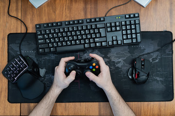 a man holds a game pad around a gaming keyboard in his hands, a game pad mouse. top view © KoshkinS