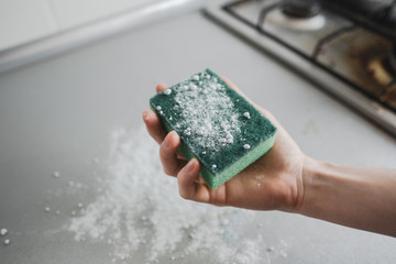 Green sponge with a cleaning powder in hand, closeup.