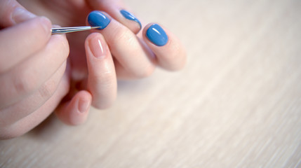 Young woman applying nail polish with brush from bottle, polishing painting fingernails with blue color enamel, doing manicure at home, perfect healthy nails care. close up view