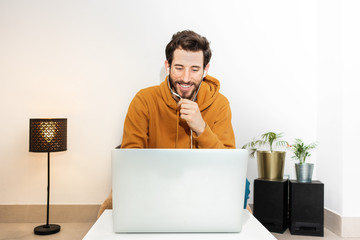 smiling man working from home with his laptop talking on the headphones.