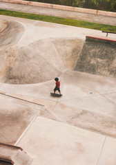 Obraz na płótnie Canvas A little boy in protection riding a skateboard at the skatepark. Urban skateboarding. Side view. Copy space