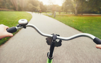First-person view of cyclist in the rainy autumn city park. Rider's hands in on a bicycle handlebar. Motion blurred