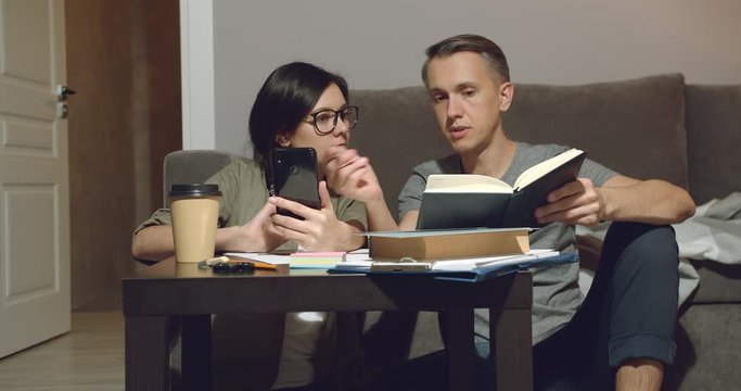 Couple discussing design of a new apartment or working together sitting on the floor and using a smartphone at home.