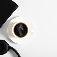 White office desk. Notebook, black headphones and coffee cup on white background.  Flat lay, top view, copy space
