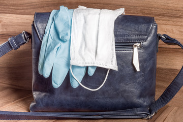 Medical mask and gloves on a handbag. Personal protective equipment and hygiene during the coronavirus infection epidemic (COVID-19).