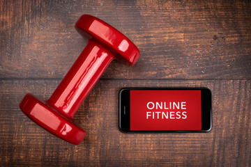 Red dumbbell and smartphone on a woodan background. App for training indoors. Online Fitness...