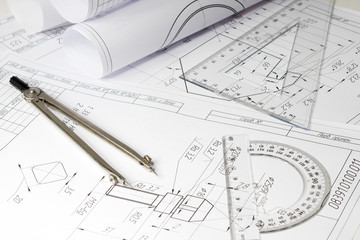 engineering drawings and rolls of drawings are on a white table, compasses, conveyor