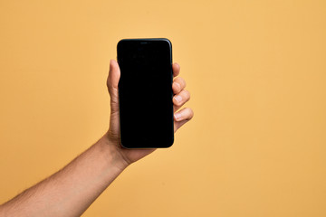 Fototapeta na wymiar Hand of caucasian young man holding smartphone showing screen over isolated yellow background