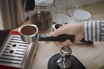 female hand holding coffee holder near coffee machine at home.