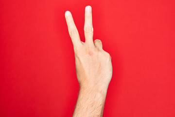 Hand of caucasian young man showing fingers over isolated red background counting number 2 showing two fingers, gesturing victory and winner symbol