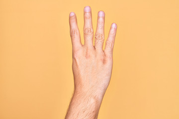 Hand of caucasian young man showing fingers over isolated yellow background counting number 4 showing four fingers
