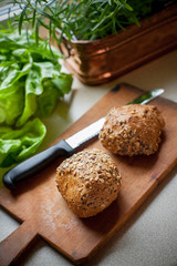 Whole grain rolls on wooden board with lettuce and herbs in background
