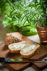 Whole grain rolls on wooden board with lettuce and herbs in background
