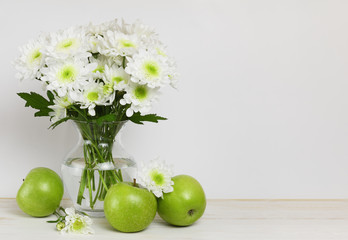 Obraz na płótnie Canvas White chrysanthemum flowers bouquet in a glass vase and green apples at wooden table