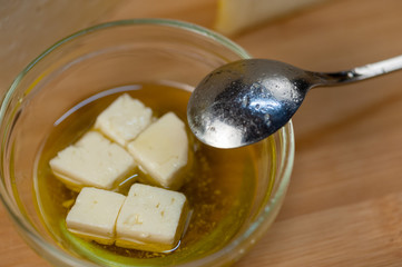 A few slices of feta cheese in olive oil in a glass bowl on a wooden board