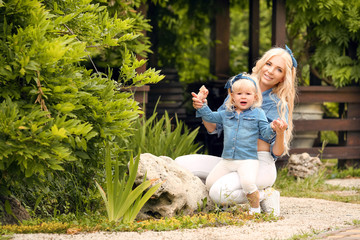Family look. Blonde Mother and daughter holding and playing on summer park. Happy family lifestyle concept. Beautiful portrait of Mom and her pretty girl in same clothes.