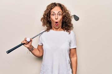 Middle age beautiful sportswoman playing golf using stick and ball over white background scared and...