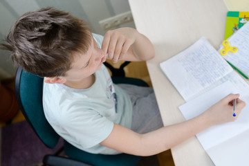 A teenager boy sits at a table in his room, doing homework.
