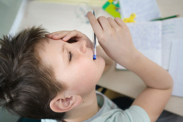 A teenager boy in his room sits at a table and does homework. Thinking. Portrait, close-up. View from above