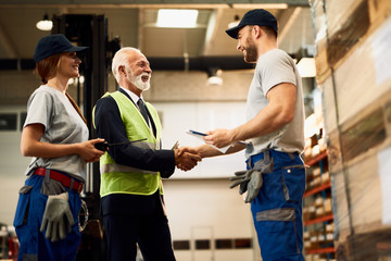 Below view of happy mature businessman shaking hands with a warehouse worker.