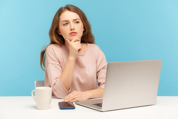 Let me think! Young pretty businesswoman with pensive thoughtful expression leaning on hand and pondering, deciding having doubts while working on laptop from home office. indoor studio shot isolated