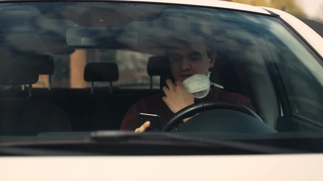 A young guy speaks by video link sitting in the car, taking off his mask to talk.
