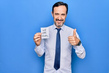 Middle age business man asking for social rights holding paper with we are equal message smiling happy and positive, thumb up doing excellent and approval sign