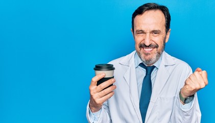 Middle age handsome doctor man wearing coat drinking cup of takeaway coffee screaming proud, celebrating victory and success very excited with raised arm