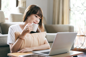 Asian teenager woman work and study online via internet at home hold coffee cup.