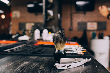 straight razor, brush for shaving beard along with bowl, blurred background of hair salon for men, barber shop
