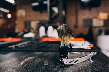 straight razor, brush for shaving beard along with bowl, blurred background of hair salon for men, barber shop