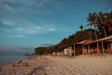 Beautiful deserted beach on the island of Bali at sunset. Rocks and nature. Plants and houses on the coast. Tropical paradise. Stones and white sand on the ocean