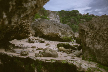 Beautiful deserted beach on the island of Bali at sunset. Rocks and nature. Plants and houses on the coast. Tropical paradise. Stones and white sand on the ocean