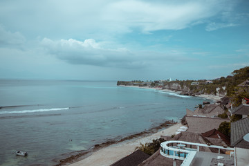 Beautiful deserted beach on the island of Bali at sunset. Rocks and nature. Plants and houses on the coast. Tropical paradise. Stones and white sand on the ocean