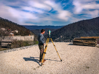 Naklejka premium A man with a total station. Surveyor man at work. Geodetic surveys during construction. Construction work on a sunny day. Set of total station and surveyor taking measurements at a construction site.