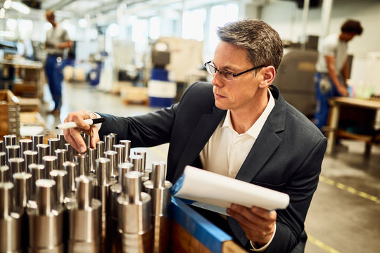 Quality control inspector examining manufactured steel cylinders in a a factory.