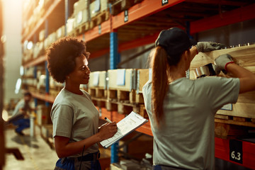 African American female inspector supervising female worker in a warehouse.