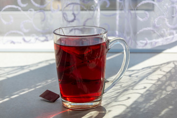 Tea in a transparent cup closeup stands at home on the table. The sun's rays shine on tea from the window, lace curtains on the window