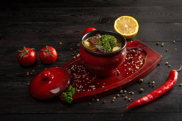 vegetable stew with potatoes and meat in a pot on a dark wooden background